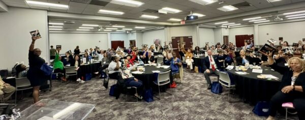 Attendees at the Hampton Roads Chamber Home-Based Business event holding up copies of Steve Waddell's book, "Valuepreneurs," in a large conference room.