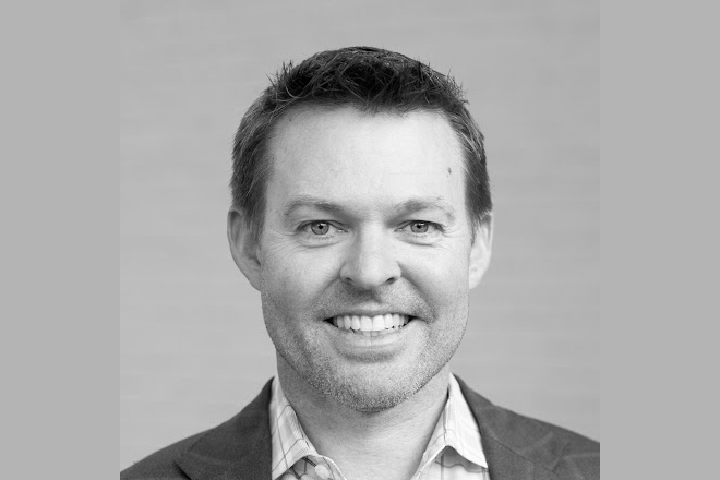 Black and white headshot of Paul Nolde, Managing Director of 757 Collab, smiling and wearing a blazer and collared shirt.